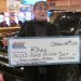 Person holding a large check in front of a vehicle they won